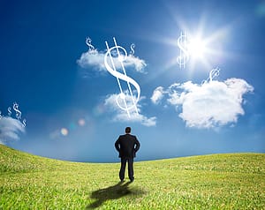 Businessman looking up at dollar signs in the sky